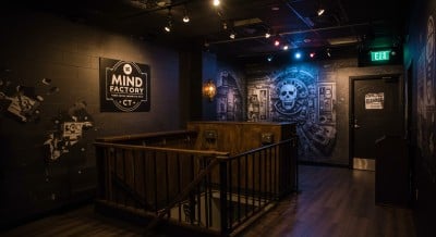 A dark, industrial-themed escape room entrance with a wooden staircase